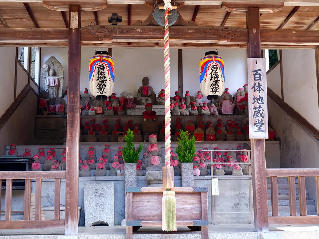 Des dizaines de petites statues de pierre coiffées de bonnets rouges, alignées sous l'auvent d'un temple